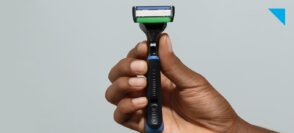 Foto de mão de homem negro segurando o aparelho de barbear The Razor 6, da Dr. JONES, em fundo neutro.